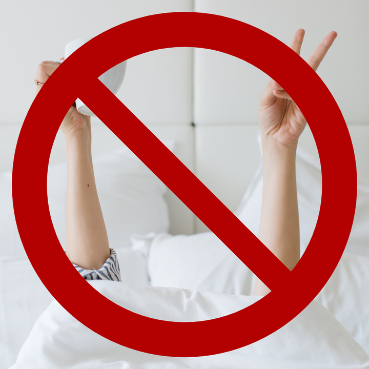 woman lying in bed with arms in the air coffee cup in one hand, piece sign with the other hand, red cross overlayed