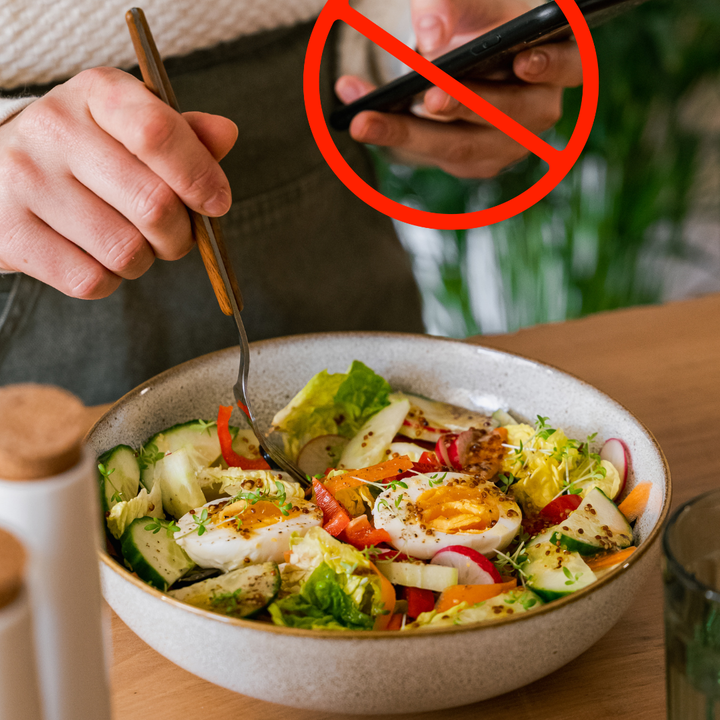 Bowl of salad with a fork in it while the eater holds a phone, a cross is over the phone