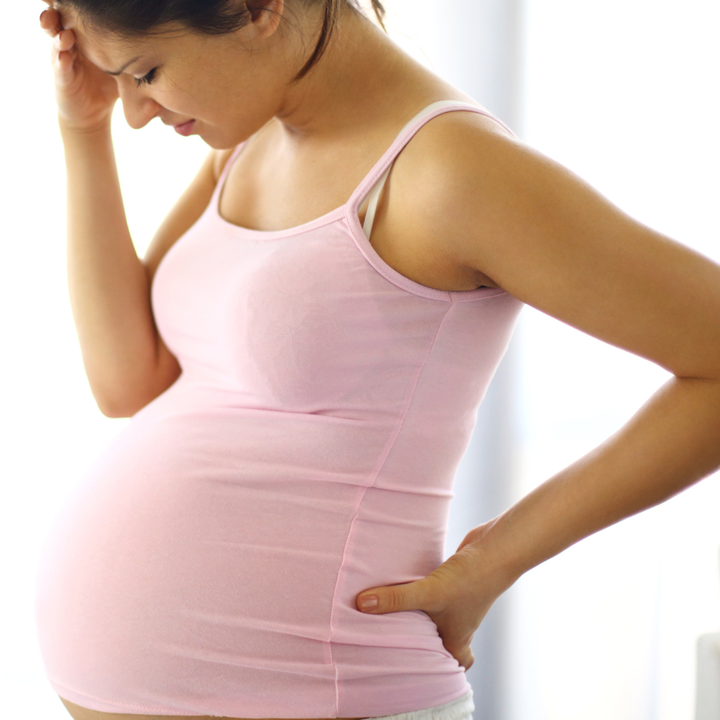 Heavily Pregnant womans profile while she holds her head with pained expression.