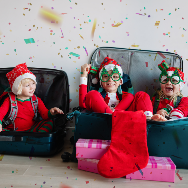 three children sit in suitcases while dressed up in Christmas clothes