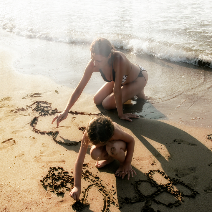 Woman and child draw pictures in the sand at the shoreline