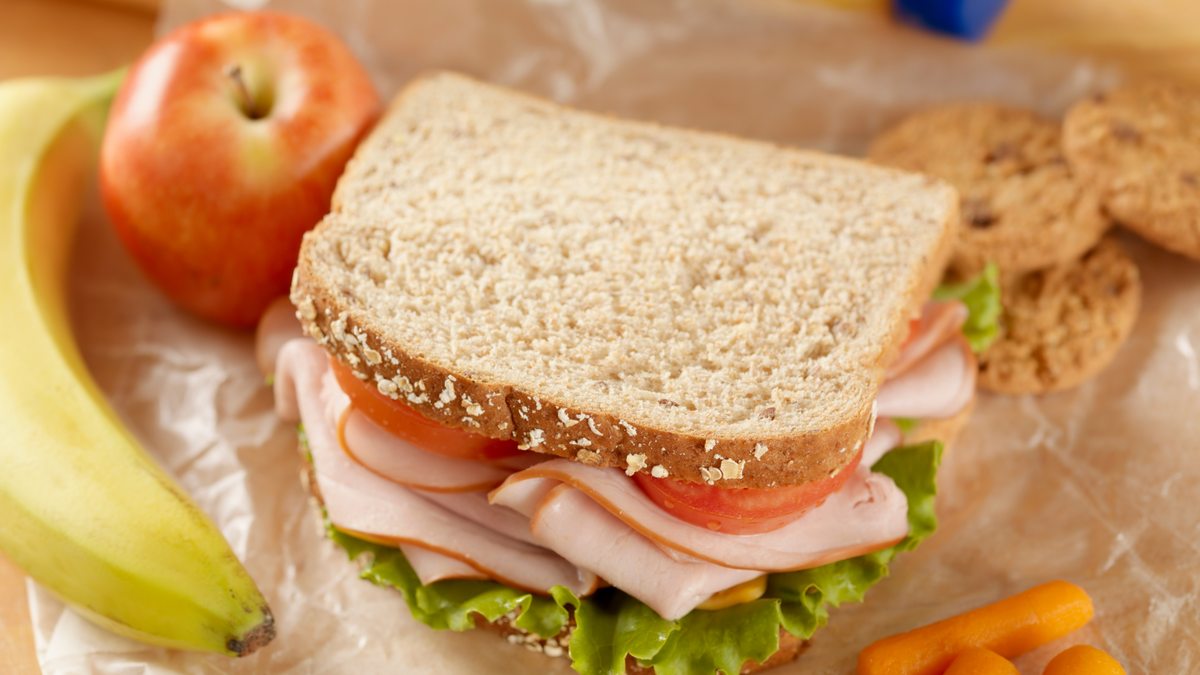 Ham and Salad sandwich sitting beside an apple and banana with some cookies