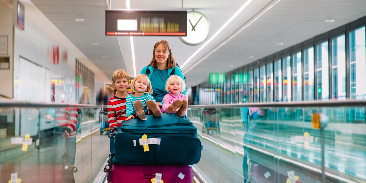 A mother pushes luggage trolley with three young children sitting on top